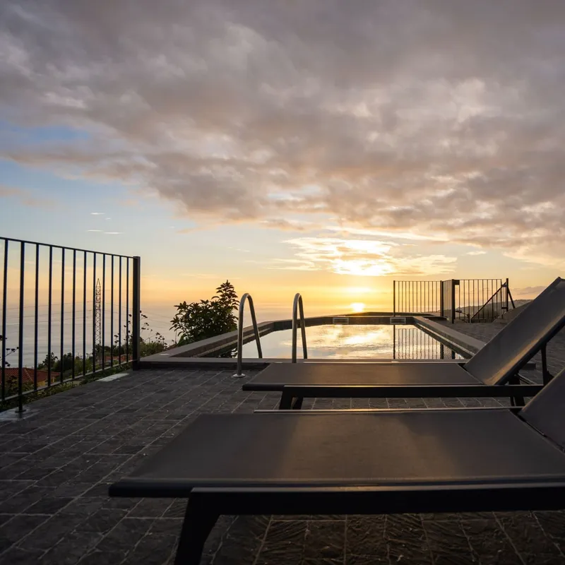 Espreguiçadeiras e piscina ao pôr do sol