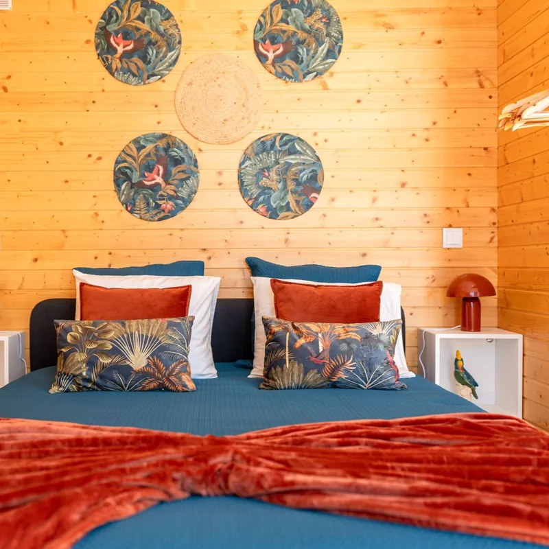Cama queen com almofadas tropicais e candeeiros cor de tijolo