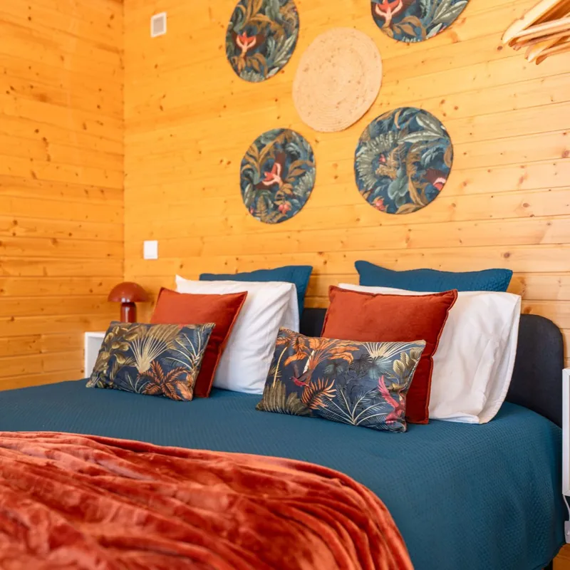 Cama com colcha azul, almofadas tropicais e quadros redondos na parede